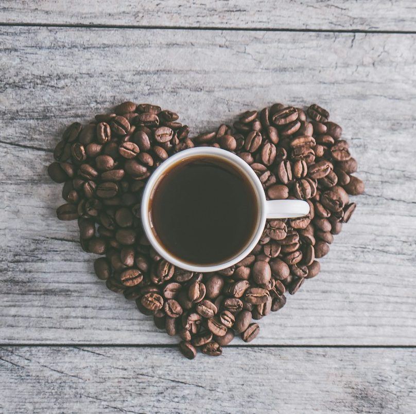 coffee filled white ceramic mug beside brown coffee beans on beige wooden surface