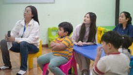 Adults and children sitting in a classroom setting.