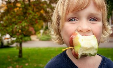 Young child with a bitten apple in mouth