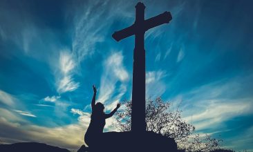 a person reaching up to a cross on a hill