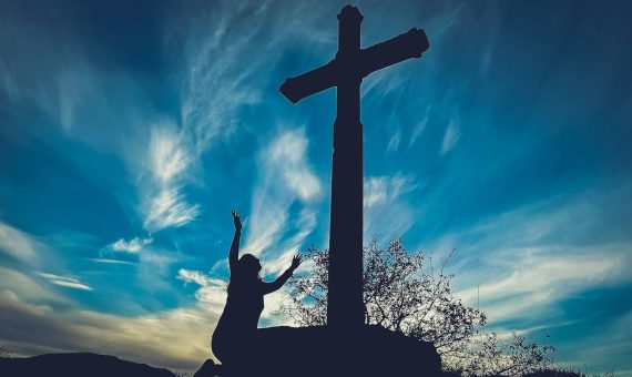 a person reaching up to a cross on a hill